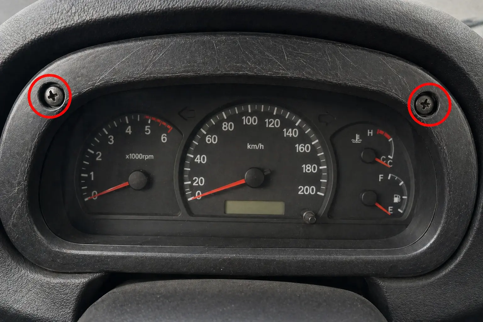 Instrument cluster bezel with scratches and misaligned screws — physical indicators of odometer tampering during disassembly